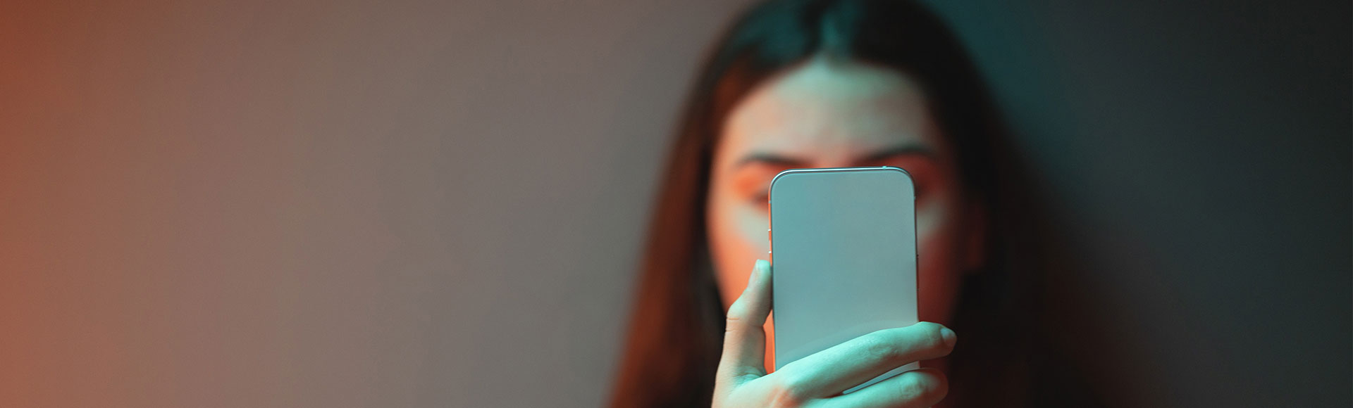 Trail BC Person holding a smartphone in front of their face with a blurred dark background and soft lighting.