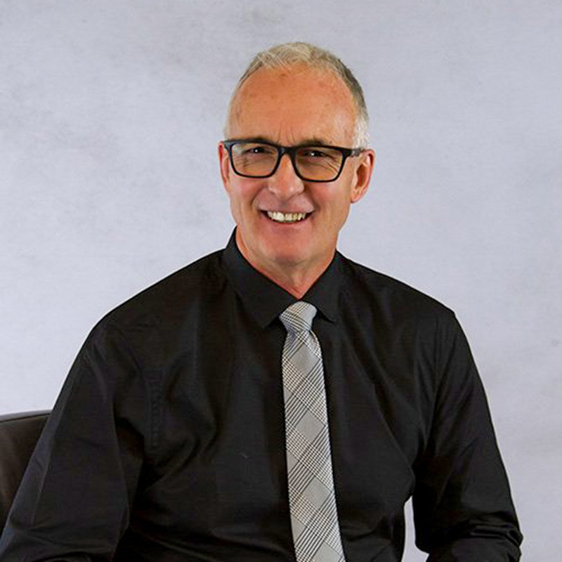 NickCashol2022 Middle-aged man with short gray hair and glasses, wearing a black shirt and gray patterned tie, smiling seated