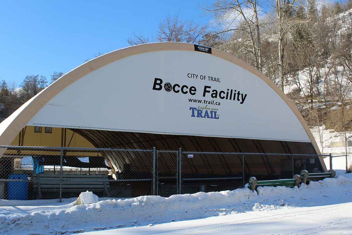 Covered bocce facility with a curved roof, surrounded by a chain-link fence and snow-covered ground.