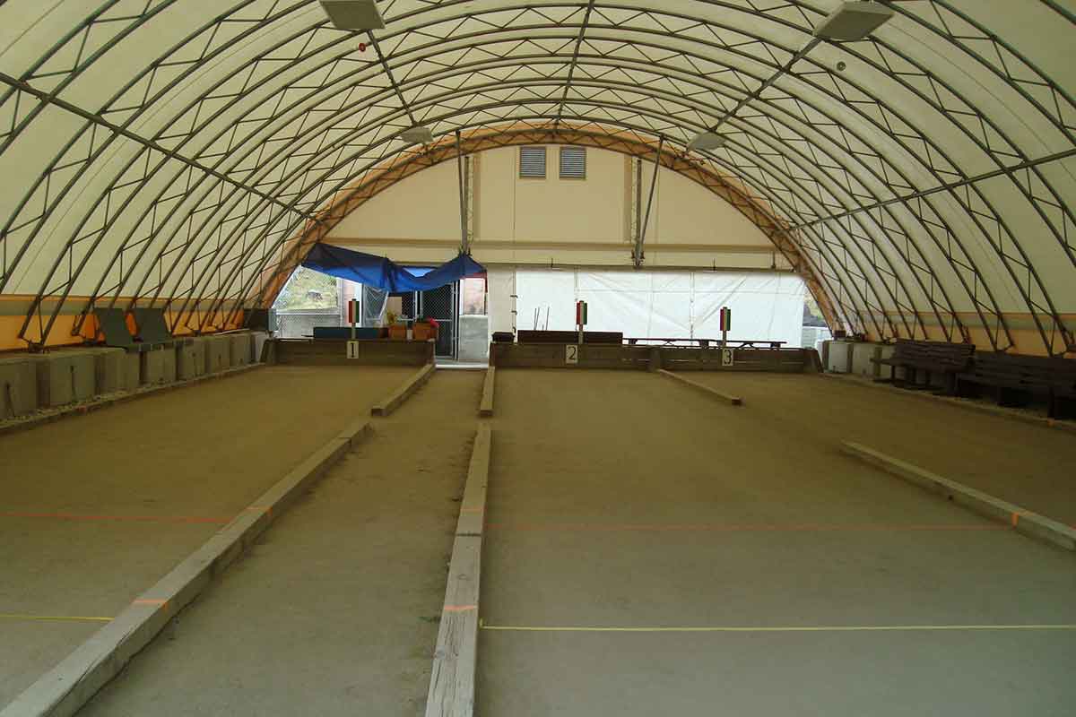 Indoor bocce ball courts under a large white fabric dome with wooden borders and numbered scoreboards.