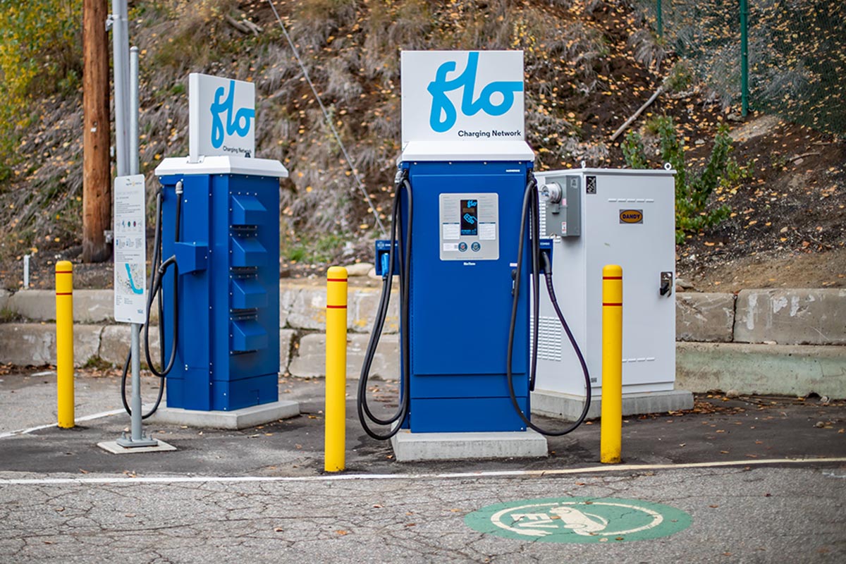 FLO charging Two blue FLO electric vehicle charging stations with cables in an outdoor parking area with yellow bollards.