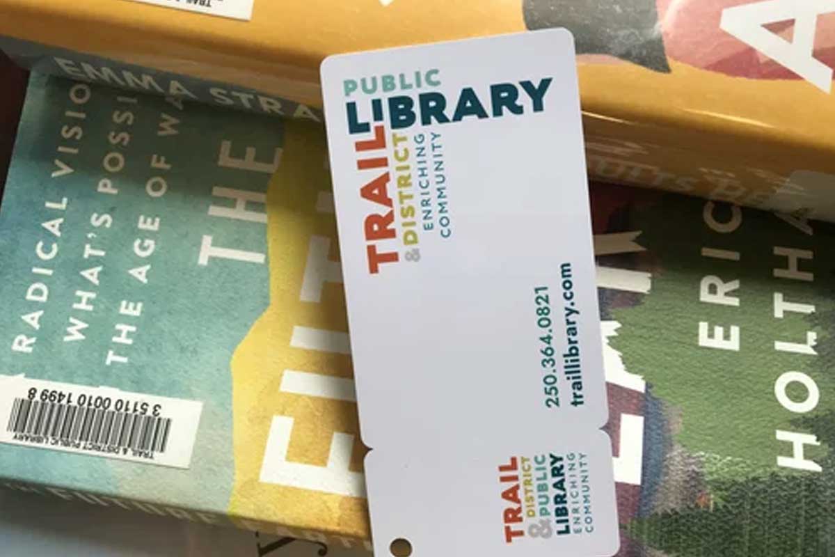 Get a library card Trail & District Public Library card resting on top of several books with visible titles and barcodes.
