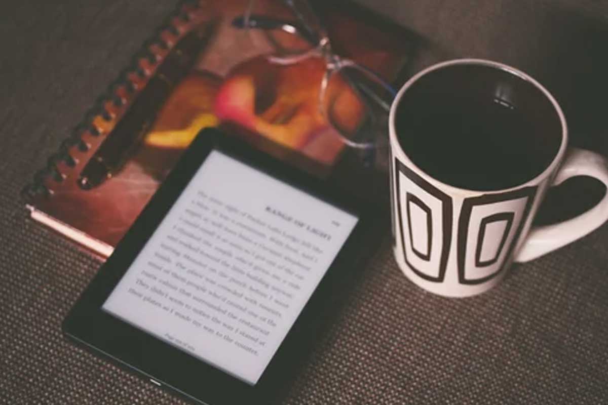 Tech Coaching E-reader displaying text, eyeglasses, a patterned coffee mug, and a closed notebook on a textured surface.
