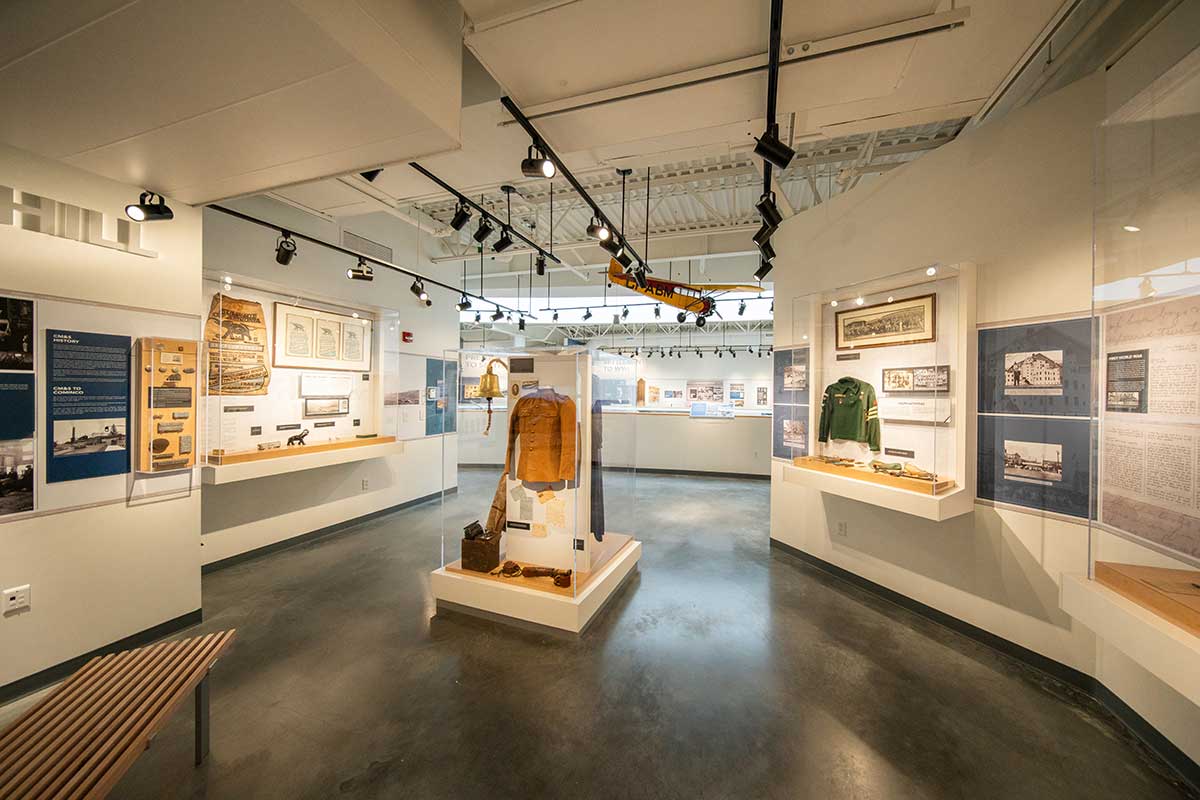 Gallery room with historical exhibits including clothing, documents, and artifacts displayed in glass cases and on walls