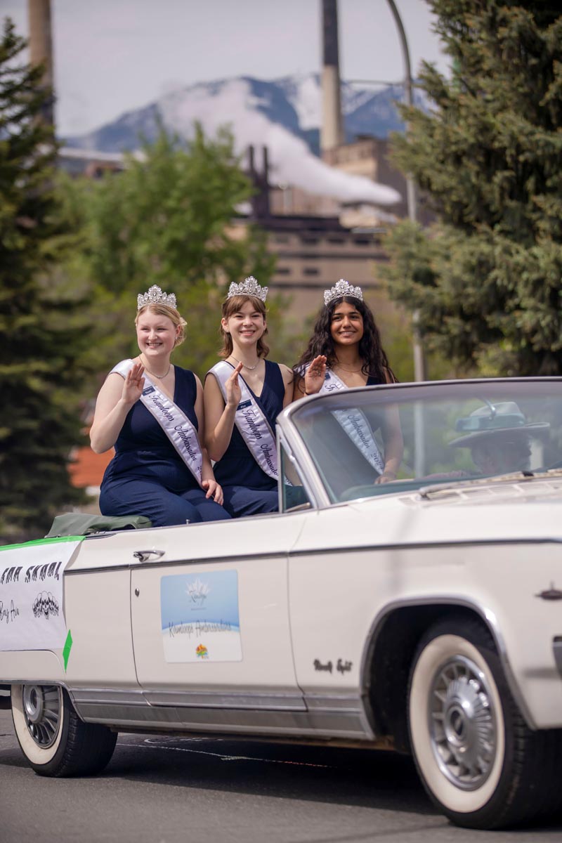 SCD Gallery_02 Three women wearing tiaras and sashes wave from the back of a white convertible car in a parade.