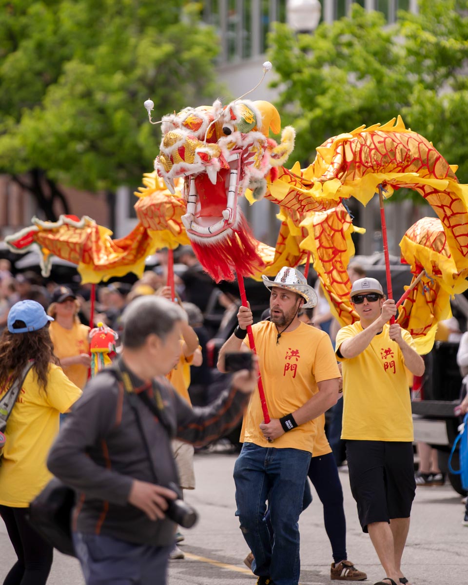 SCD Gallery_06 People in yellow shirts carrying a large yellow and red Chinese dragon puppet during a street parade with onlookers.
