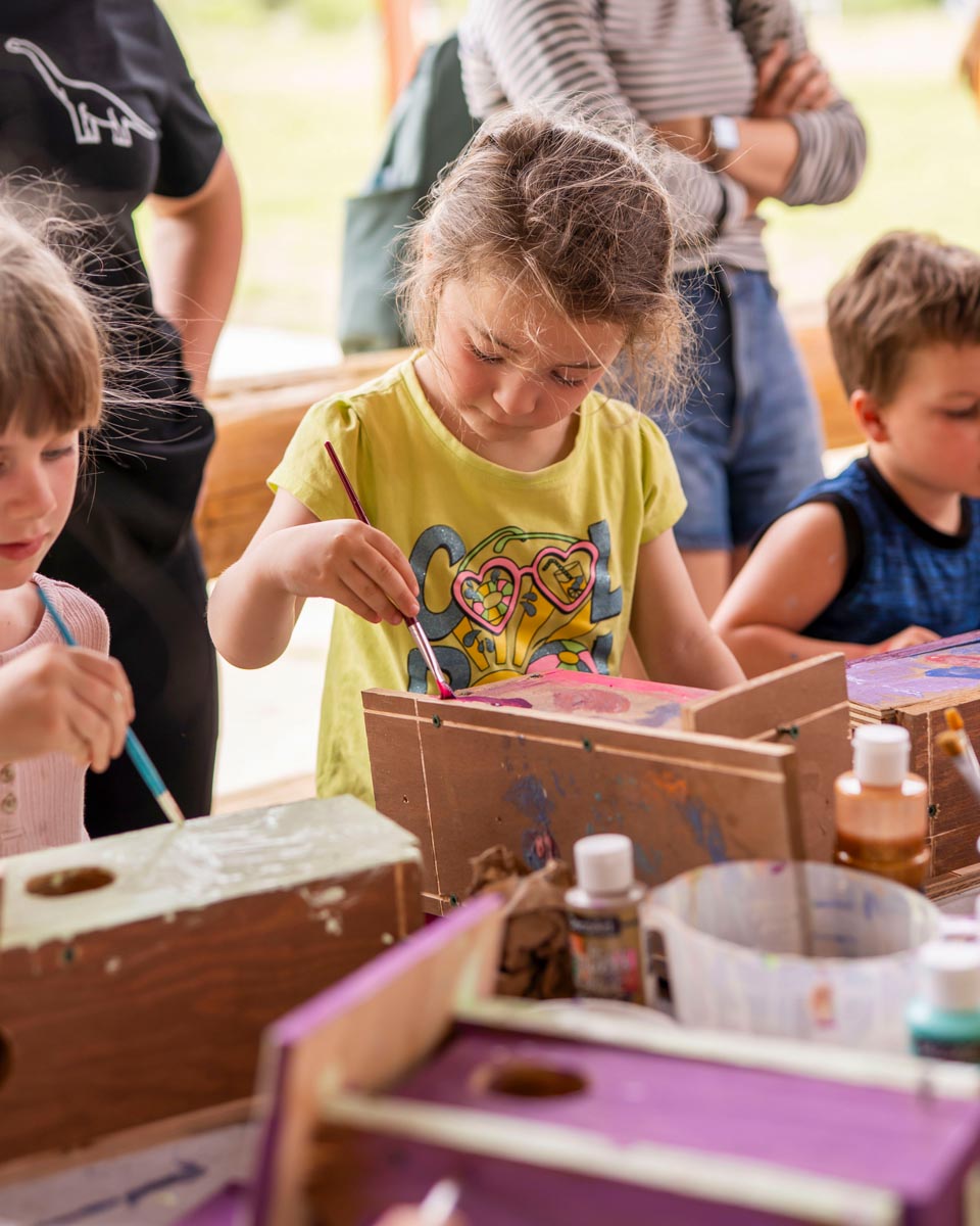SCD Gallery_10 Children painting wooden birdhouses at a table with paint bottles and brushes during an outdoor event.