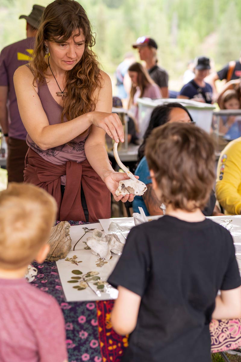 SCD Gallery_11 Woman showing animal bone to two children at a table with natural objects during an outdoor event
