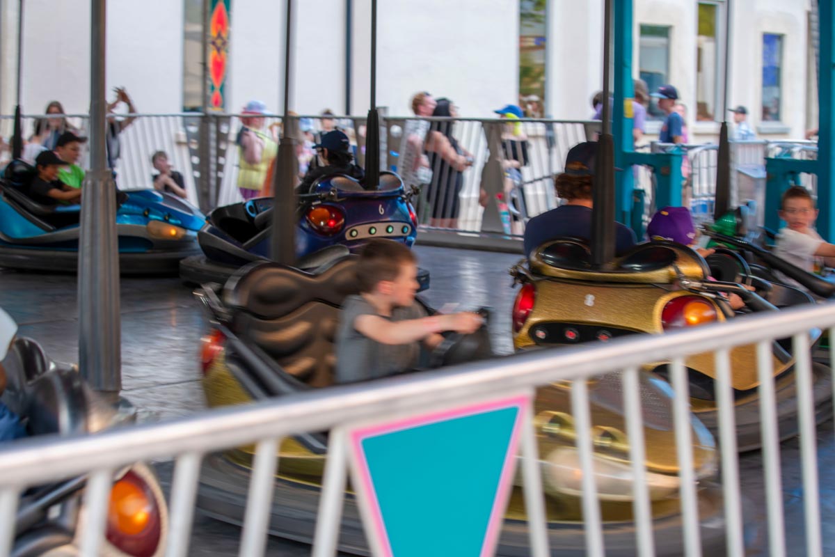 SCD Gallery_15 Children and adults riding bumper cars at an outdoor amusement ride with spectators behind a fence