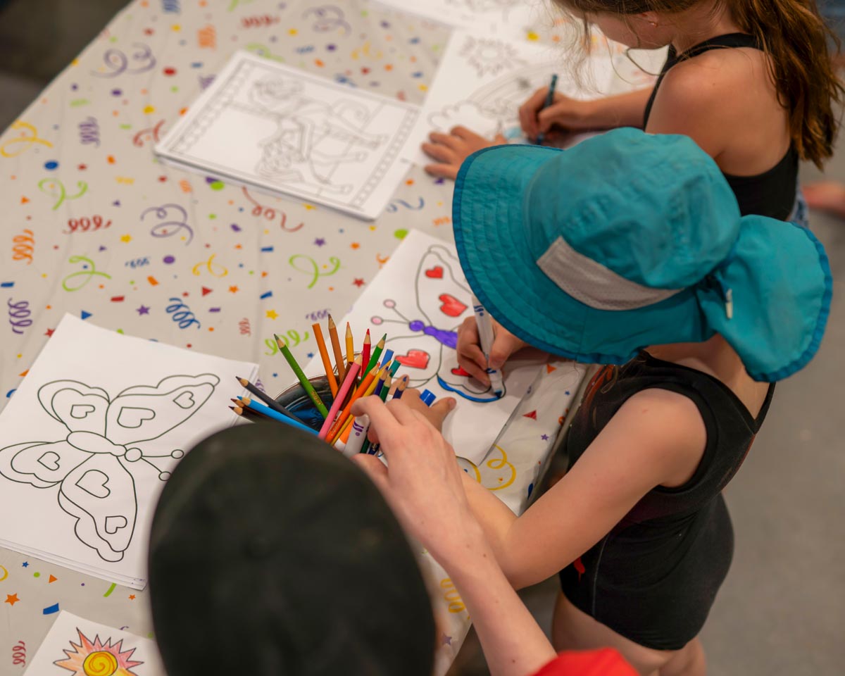 SCD Gallery_17 Children coloring butterfly drawings at a table with colored pencils and a festive tablecloth