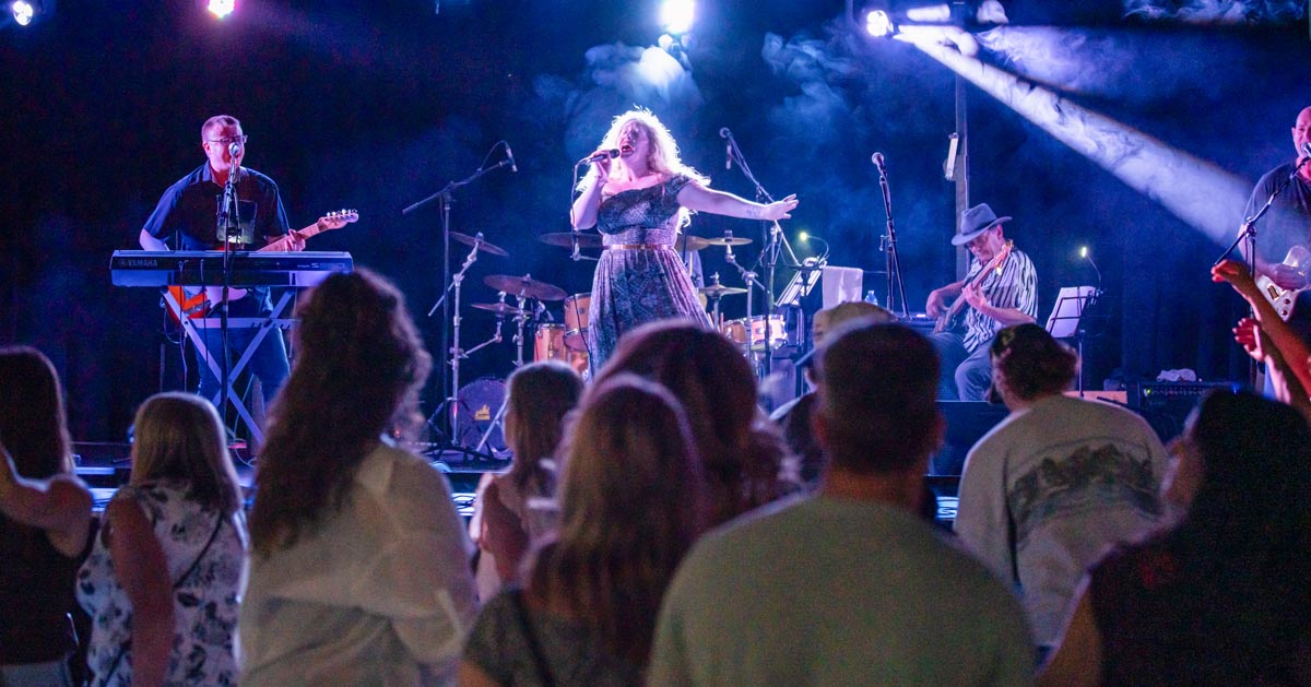 SCD Gallery_25 Band performing on stage with a female singer, keyboardist, and guitarist, audience watching in foreground at night.